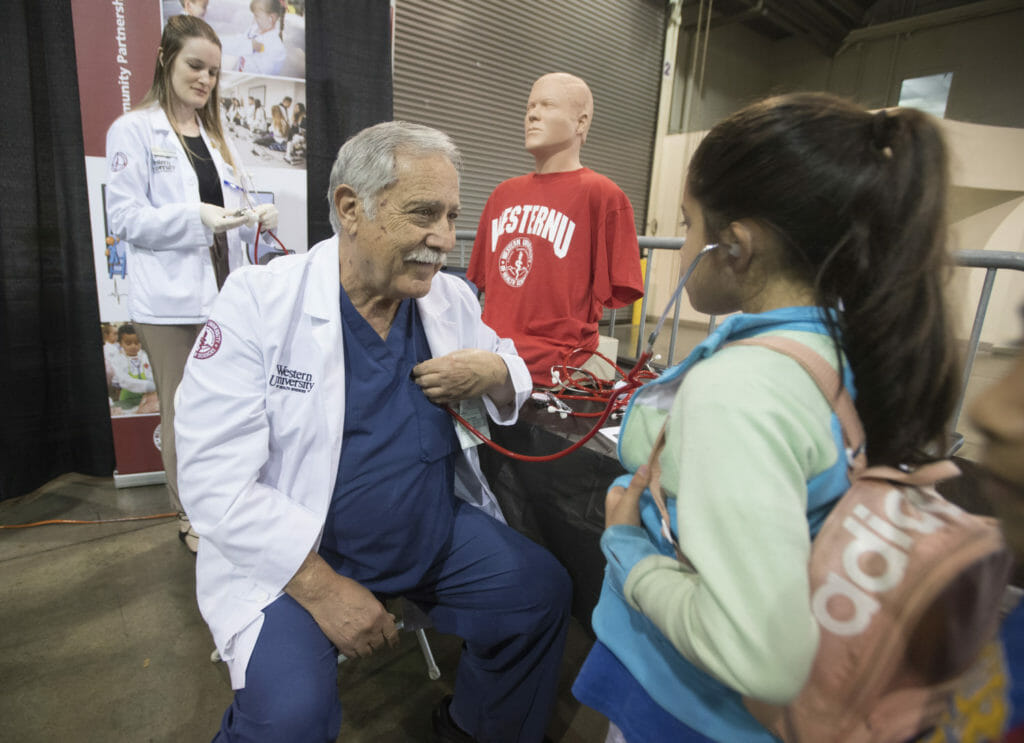 College of Health Sciences MSPA student Natasha Granneman and Assistant Teacher Oscar Norona, PA-C, teach a student how to use a stethoscope at the STEAM Fair. Photo courtesy of Tom Zasadzinski, Cal Poly Pomona.