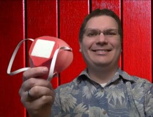 WesternU College of Optometry Associate Professor Joshua Cameron holds a red 3D printed mask in his right hand. 