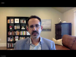 Screenshot of Dr. Asaf Bitton, who is wearing glasses and a blue suit, with a bookshelf in the background.