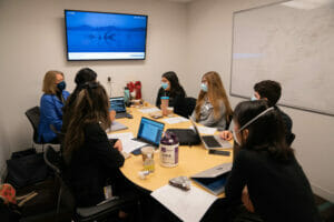 Study room with seven people sitting at a conference table. Screen mounted on the wall. White board on another wall.