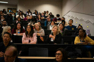 Several audience members seated in a large lecture hall with one person speaking into a microphone.