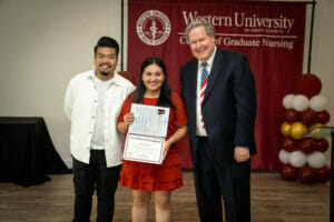 Three people standing together, the woman in the center holding a certificate.