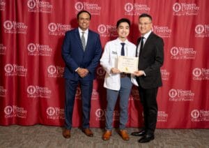 Three men pose for a photo at Western University College of Pharmacy. The man in the center holds a certificate.