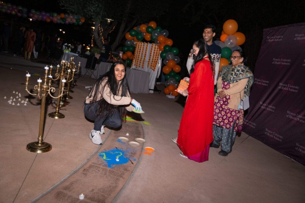 People engage in a colorful art activity on the ground during an outdoor event, surrounded by candles and balloons.