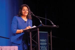 A person in a blue suit speaks at a podium labeled "Pharmacy Education 2024" against a blue background.