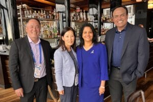 Four people standing together in a bar, smiling at the camera. They are dressed in formal attire.