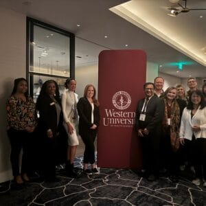 A group of people stand smiling next to a banner for Western University of Health Sciences in a modern hallway.