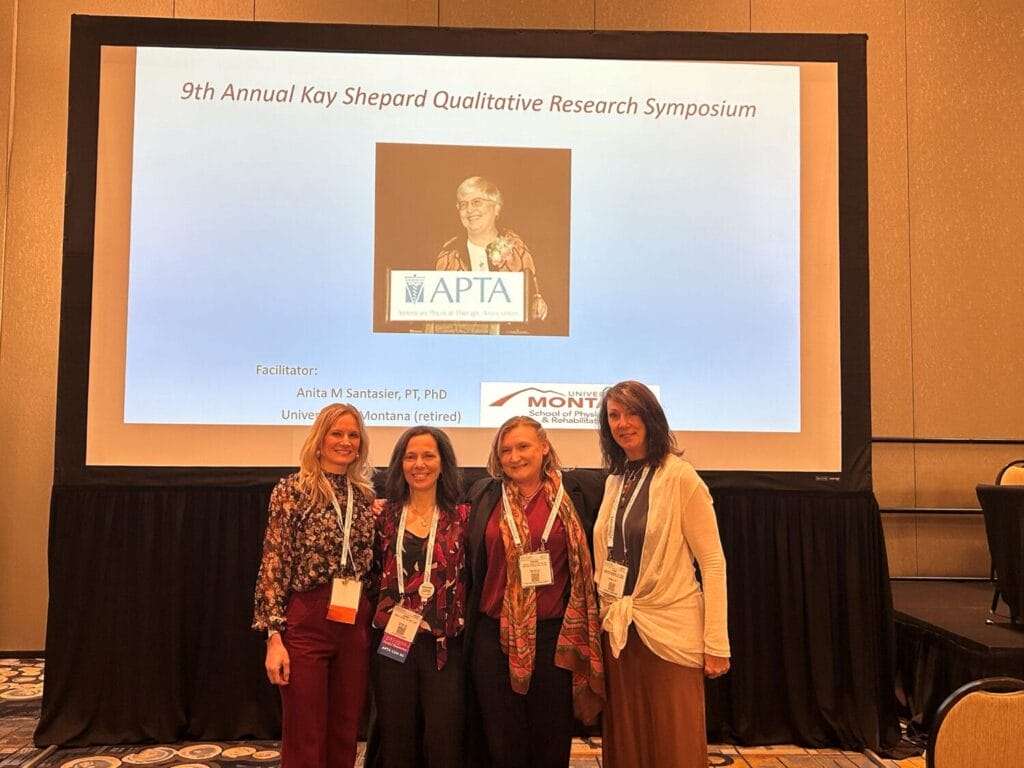 Four people stand smiling in front of a presentation screen at the 9th Annual Kay Shepard Qualitative Research Symposium.