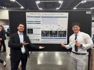 Two men in formal attire stand in front of a scientific poster titled "Under the Surface: Correlates with Maxillary Sinus Shape" at a conference, smiling and gesturing toward the poster.