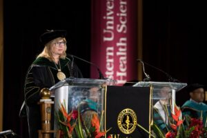 A woman in academic regalia speaks at a podium during a commencement ceremony at Western University of Health Sciences.