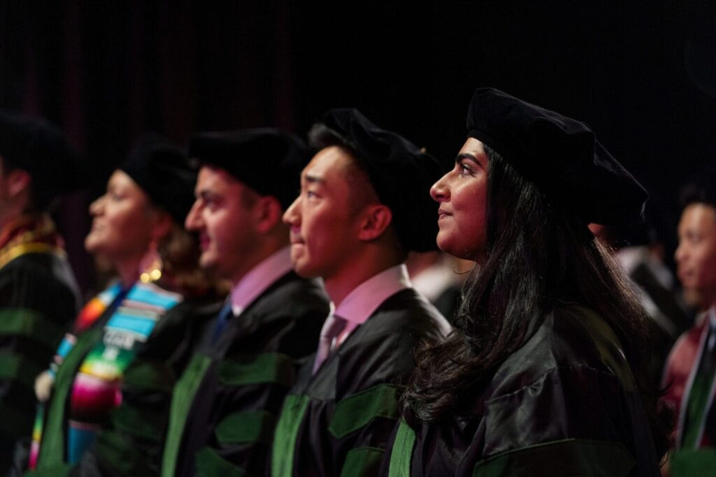 A group of graduates in caps and gowns sit in a row, facing forward during a commencement ceremony.