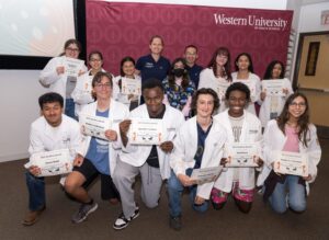 A group of students in white coats hold certificates while posing for a photo with instructors at Western University of Health Sciences.