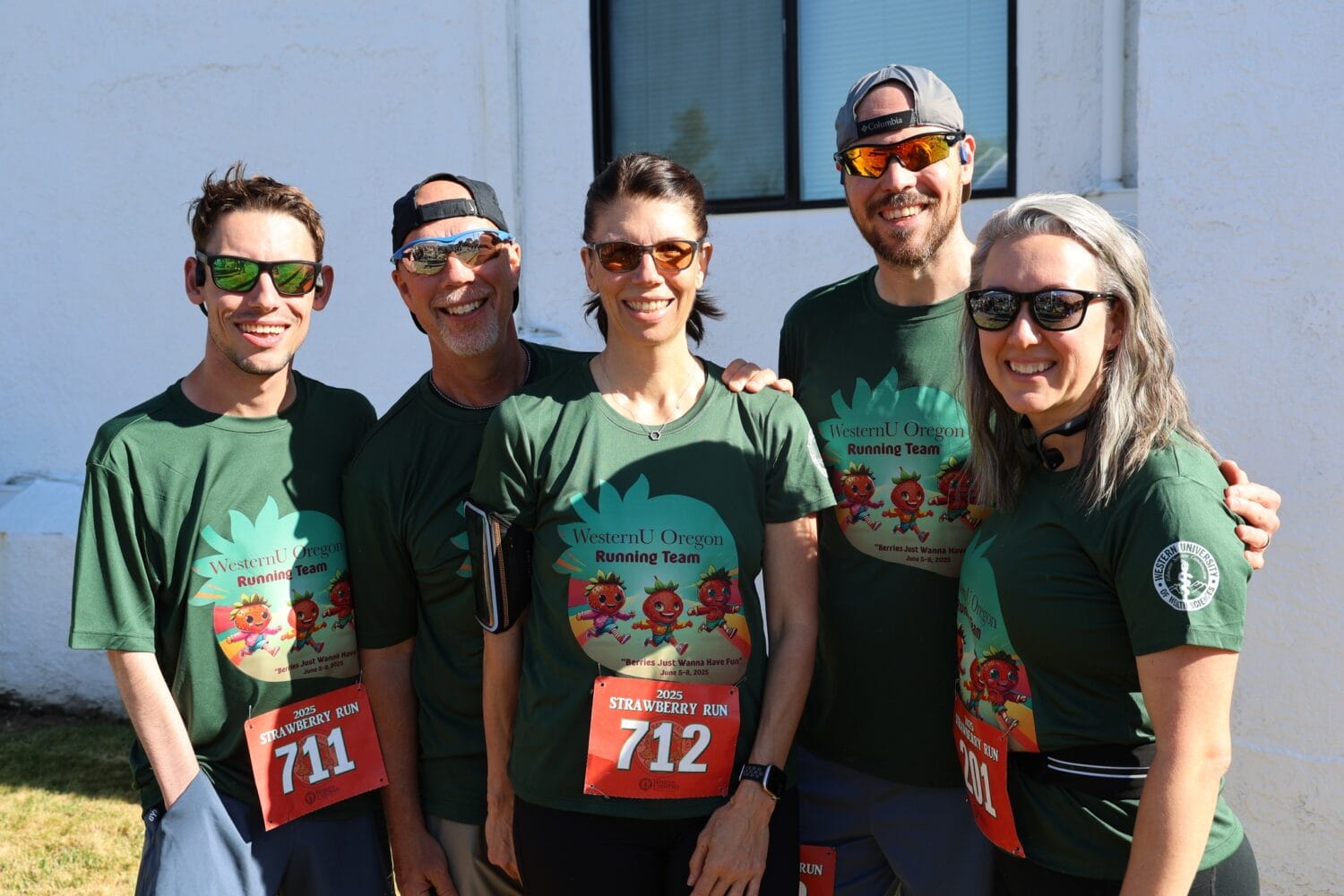 Five people wearing matching green "WesternU Oregon Running Team" shirts and race bibs stand outdoors, smiling at the camera.