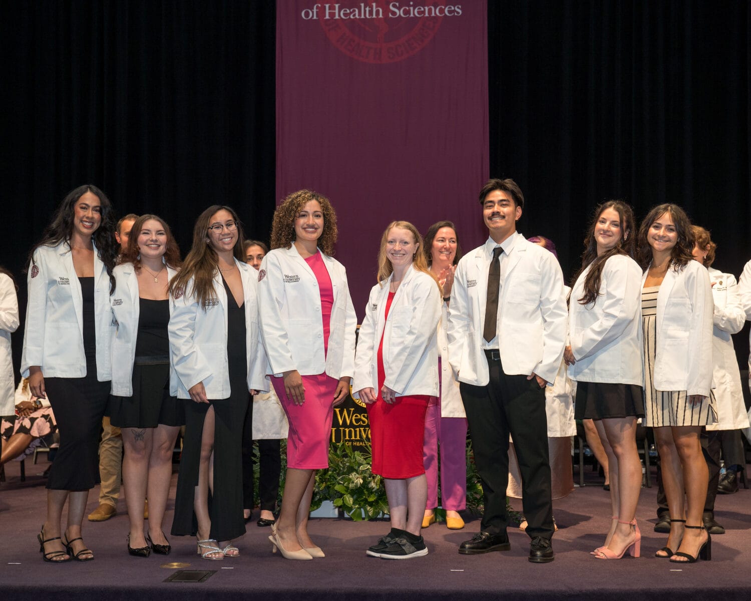 A group of people in white coats stand on stage, smiling for a photo during a ceremony at Western University of Health Sciences.