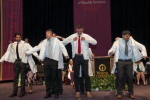 Four individuals are helped into white coats on stage during a ceremony at Western University, with an audience and university signage in the background.