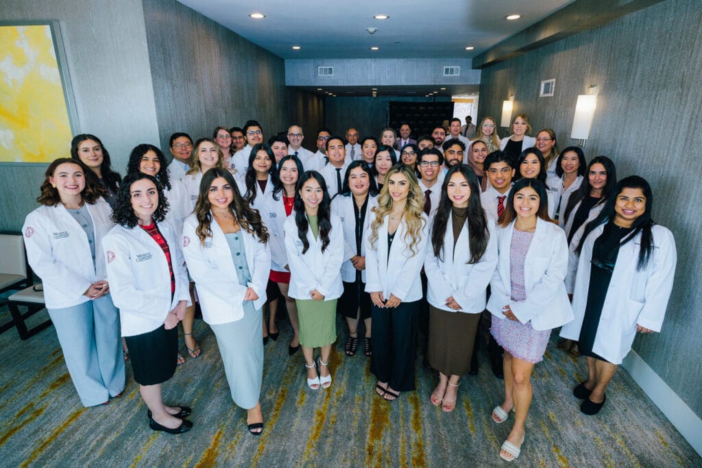 A large group of people, many wearing white coats, pose together in a hallway, likely for a professional or academic event.