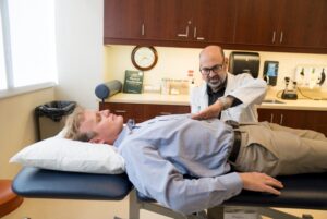 A doctor examines a male patient lying on an exam table in a medical office.