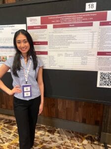 A woman stands next to a research poster about postoperative complications in foot and ankle surgery at a medical conference.