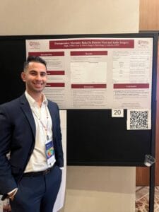 A man in a suit stands next to a scientific poster titled "Postoperative Mortality Risks In Diabetic Foot and Ankle Surgery" displayed on a black board at a conference.
