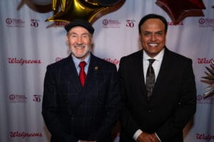 Two men in suits pose and smile for a photo in front of a backdrop featuring Walgreens and Western University College of Pharmacy logos.