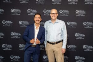 Two men stand side by side smiling in front of a Western University College of Podiatric Medicine step-and-repeat banner.