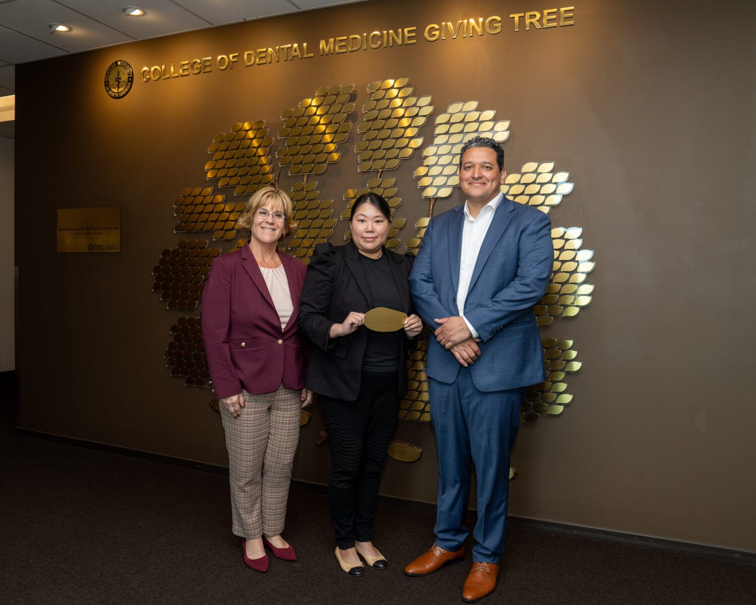 Three people stand in front of a wall display reading 
