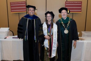 Three people in academic regalia pose for a photo at a graduation event, with two signs labeled "Western University of Health Sciences" in the background.