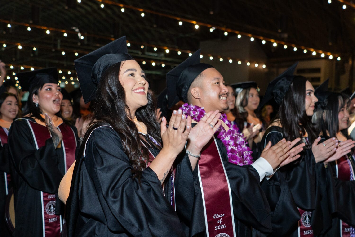 Graduates in caps and gowns applaud during a commencement ceremony, with 