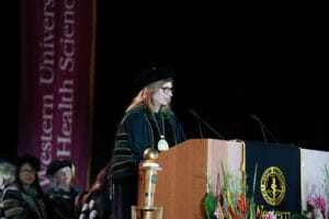 A woman in academic regalia speaks at a podium during a graduation ceremony at Western University of Health Sciences.