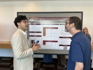 Two men converse in front of a research poster on postural sway at an academic conference; another woman stands in the background, smiling.