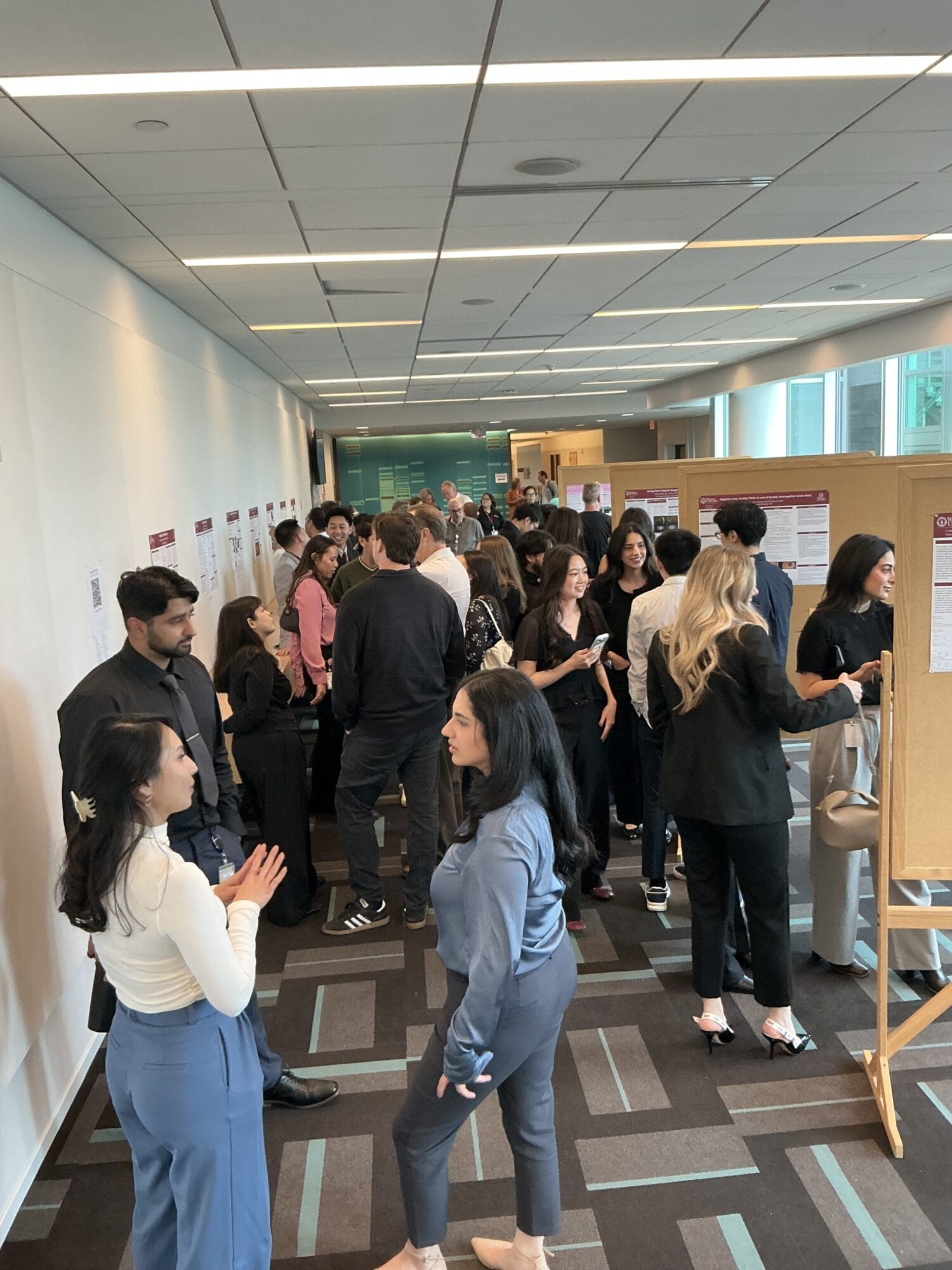 People are gathered in a hallway, standing and talking in groups next to display boards with posters on the walls.