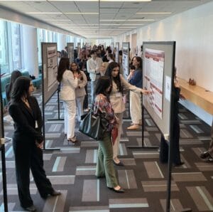 People stand and converse in a hallway lined with scientific posters on display boards during a poster presentation event.