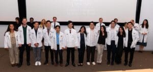 A group of students and faculty in white coats stand in front of a projector screen in a lecture hall at Western University.