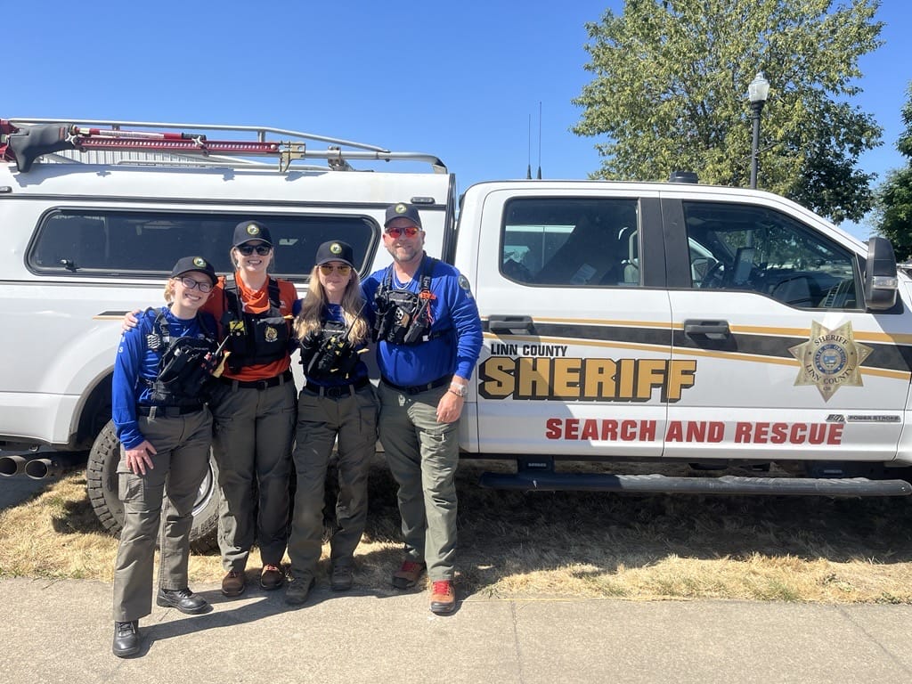 Four search and rescue team members stand in front of a Linn County Sheriff Search and Rescue vehicle on a sunny day.