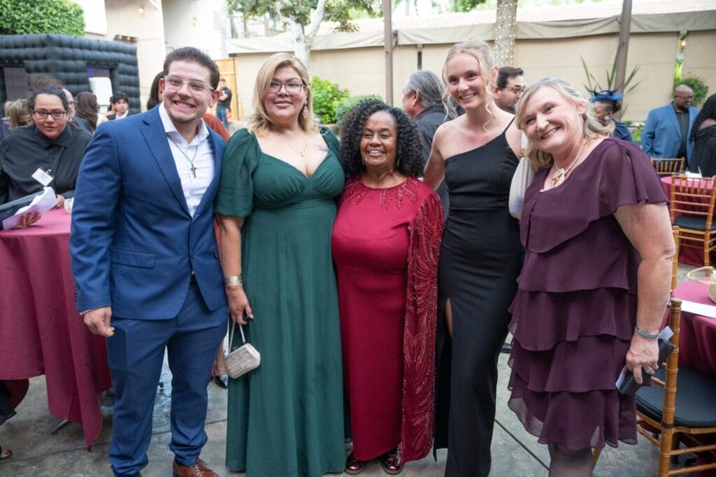 A group of five people dressed in formal attire pose together at an outdoor event, smiling for the camera.