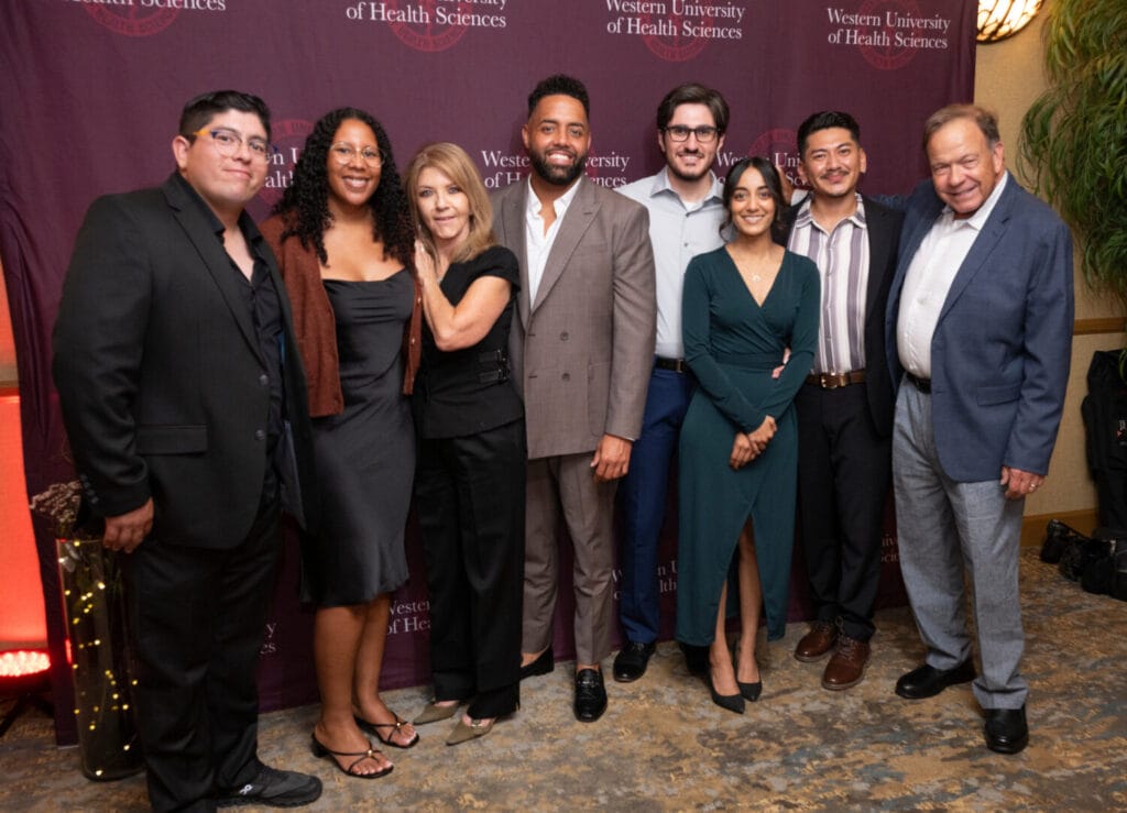 A group of seven individuals pose together at an event hosted by the Western University of Health Sciences, standing before a branded backdrop.