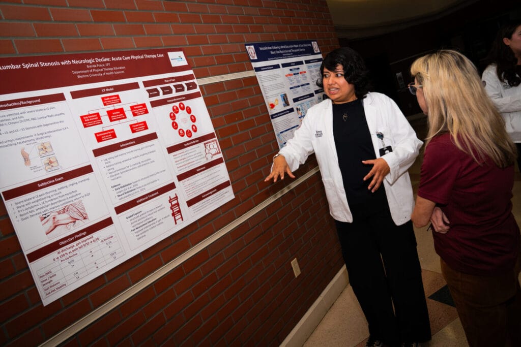 A healthcare professional in a white coat explains a research poster on lumbar spinal stenosis to an attendee during an academic presentation.