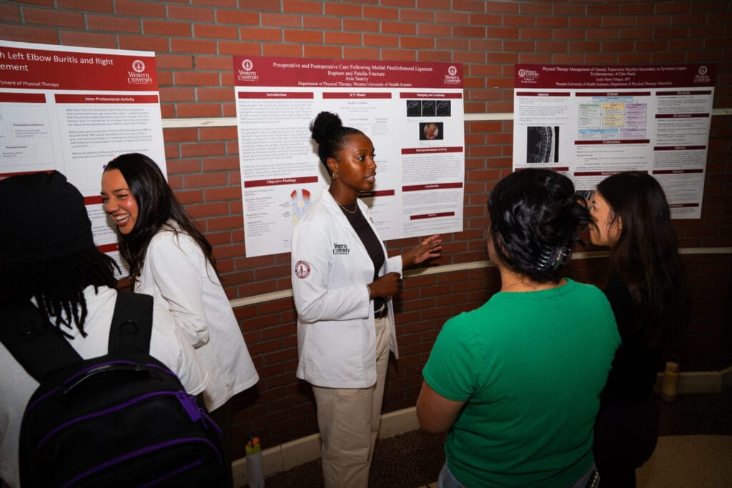 A student in a lab coat presents a research poster to an audience at a university event.