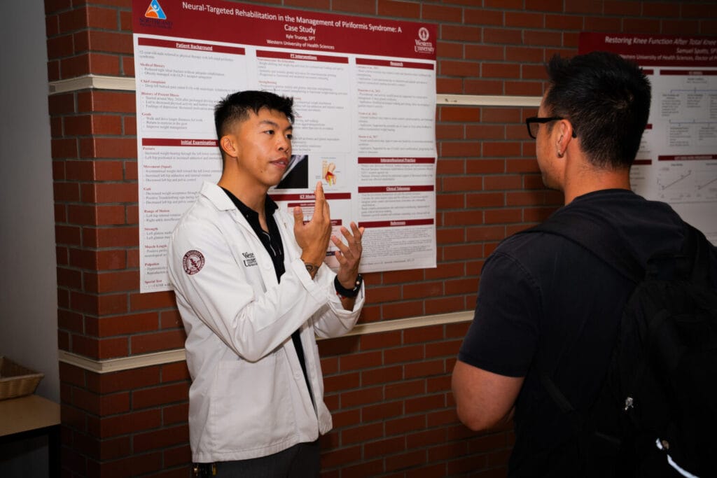 A person in a white lab coat presents a research poster to an audience member during an academic event.