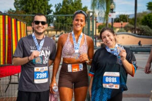 Three people wearing race medals and bibs smile for the camera after completing a running event.