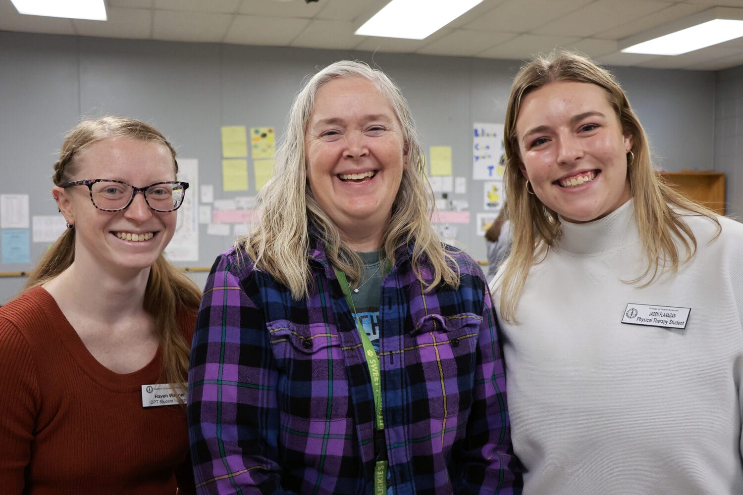 Three women smiling in an office setting, with two wearing name tags identifying them as physical therapy students.